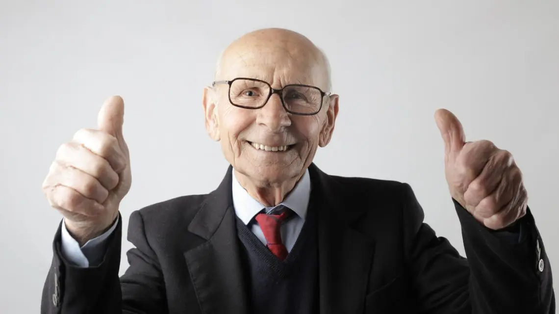 are dentures uncomfortable -- older man in a suit smiling and giving thumbs up with both hands