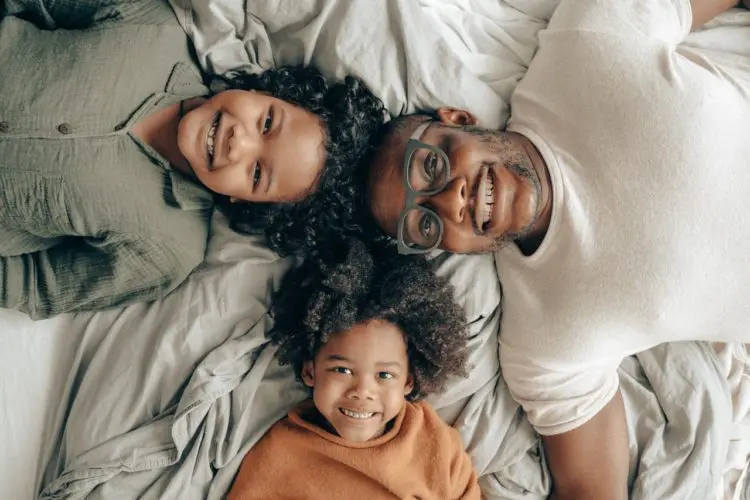 dental sealants -- African American man and two children laying on a bed, smiling at the camera
