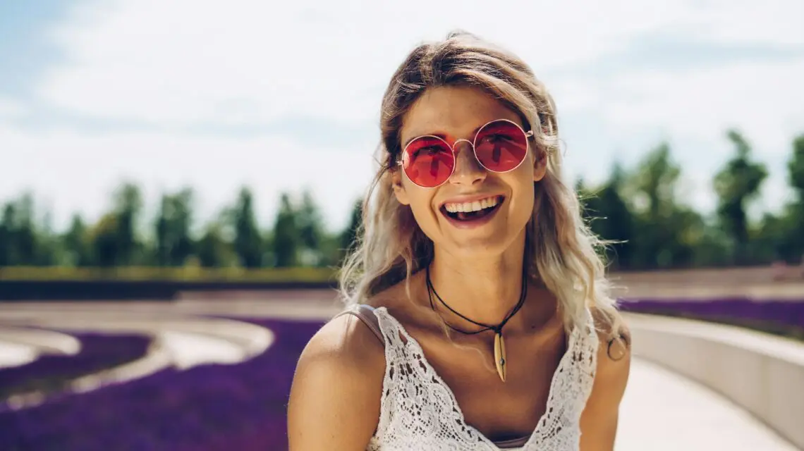 young woman smiling outside wearing pink sunglasses