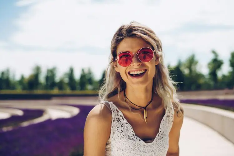 young woman smiling outside wearing pink sunglasses