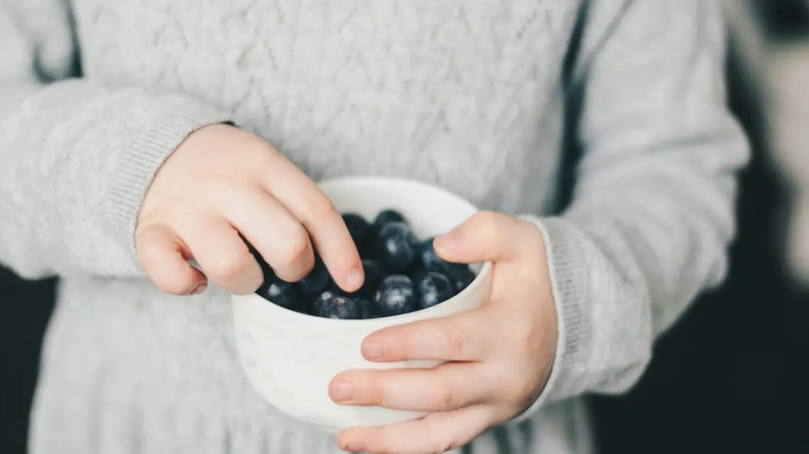 child picking blueberries out of bowl
