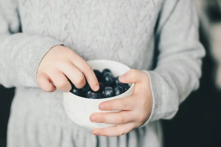 child picking blueberries out of bowl