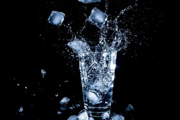 ice cubes dropped into water glass against black background