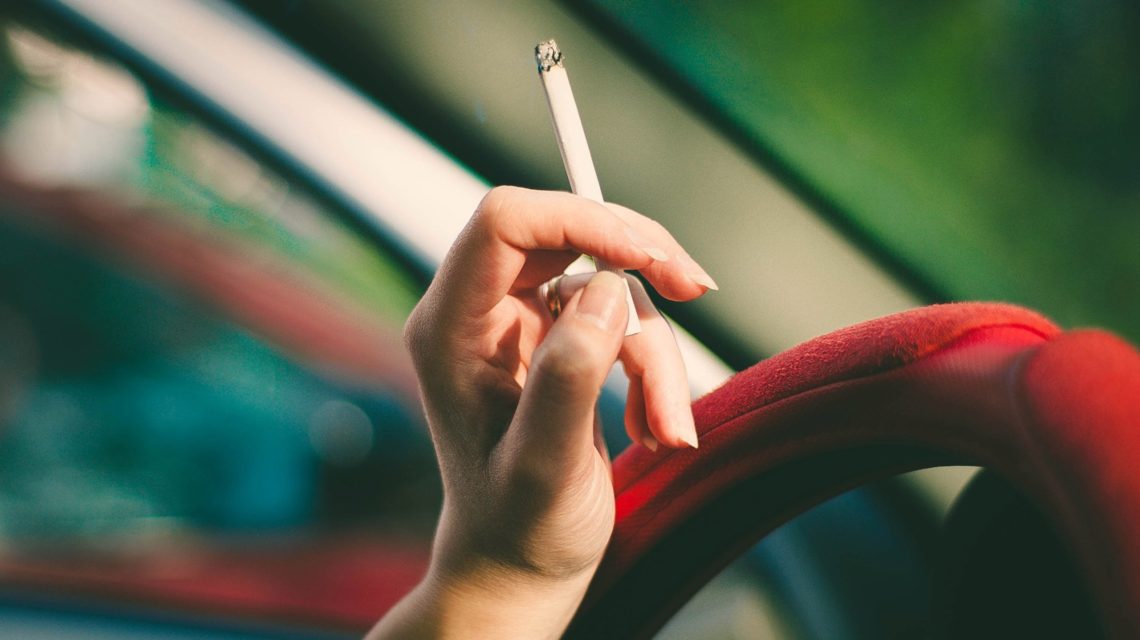 gum disease risk factors - hand holds cigarette over a steering wheel