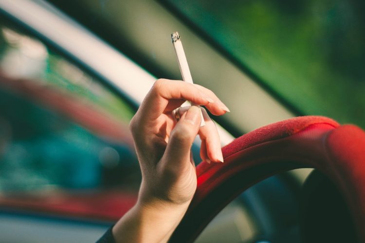 gum disease risk factors - hand holds cigarette over a steering wheel