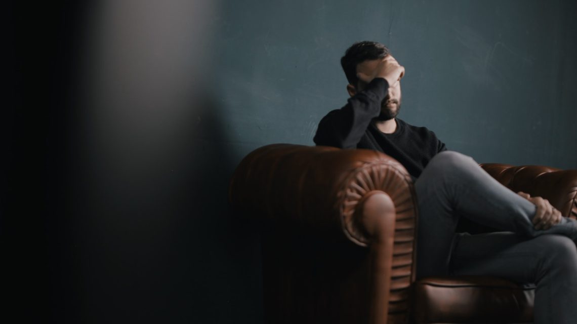 stress and oral health - man on couch with hand over face