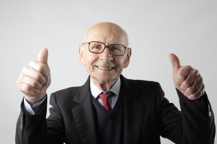 are dentures uncomfortable -- older man in a suit smiling and giving thumbs up with both hands