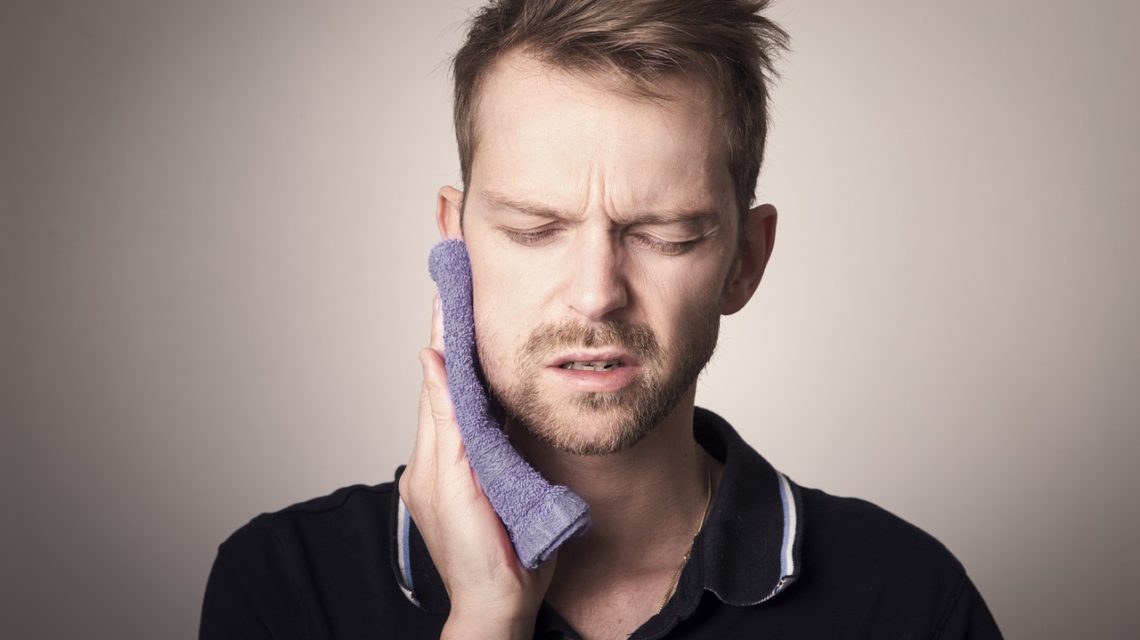 tmj tooth pain -- man holding wash cloth up to mouth in pain