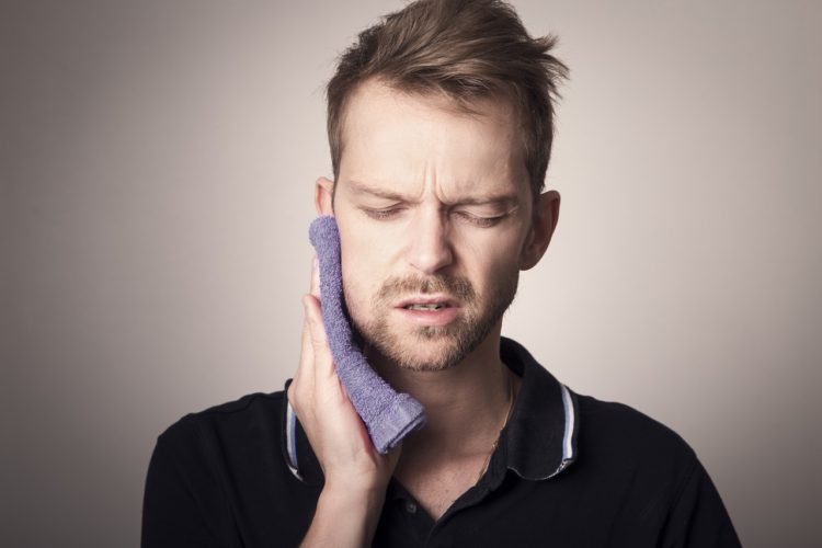 tmj tooth pain -- man holding wash cloth up to mouth in pain