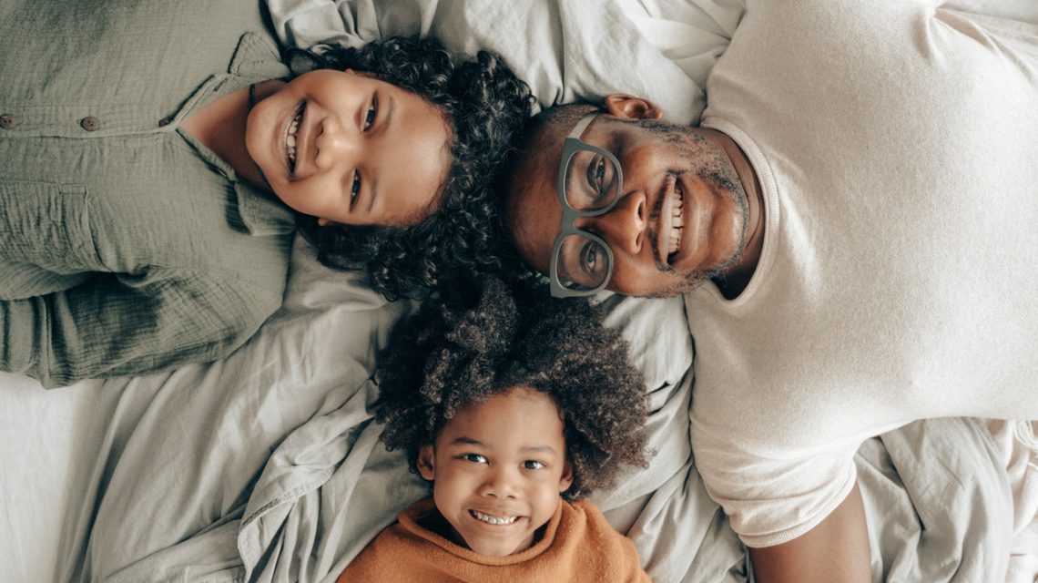 dental sealants -- African American man and two children laying on a bed, smiling at the camera