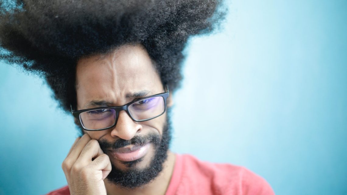 dental abscess symptoms -- African American man holding his mouth in pain