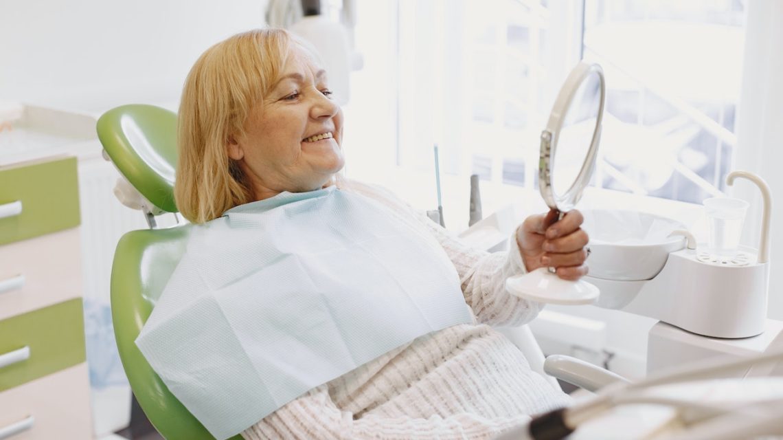 senior woman smiling looking at mirror in dentist chair