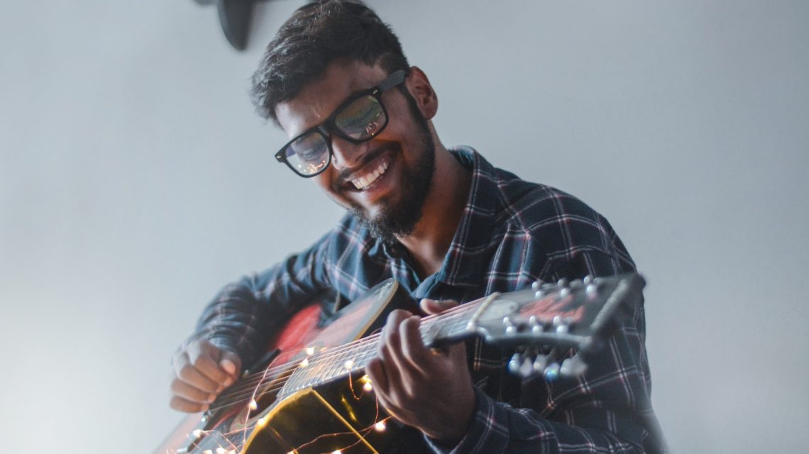 man with glasses smiling playing guitar