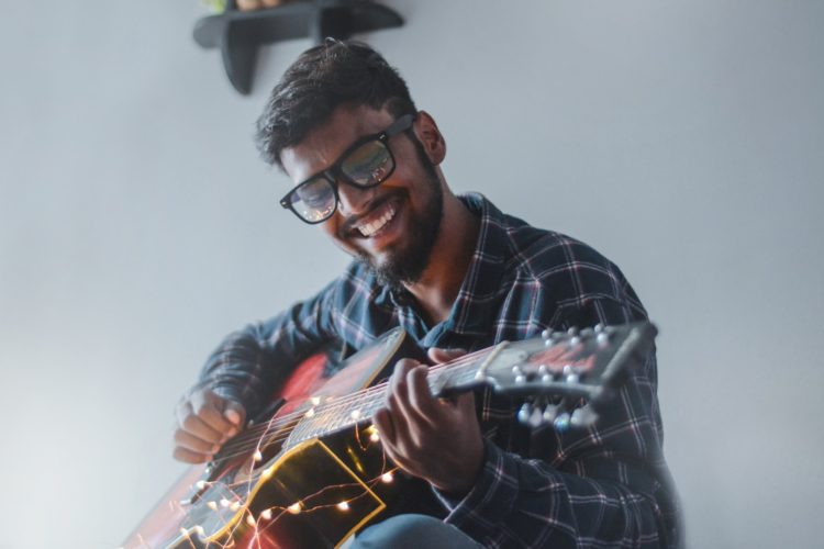 man with glasses smiling playing guitar