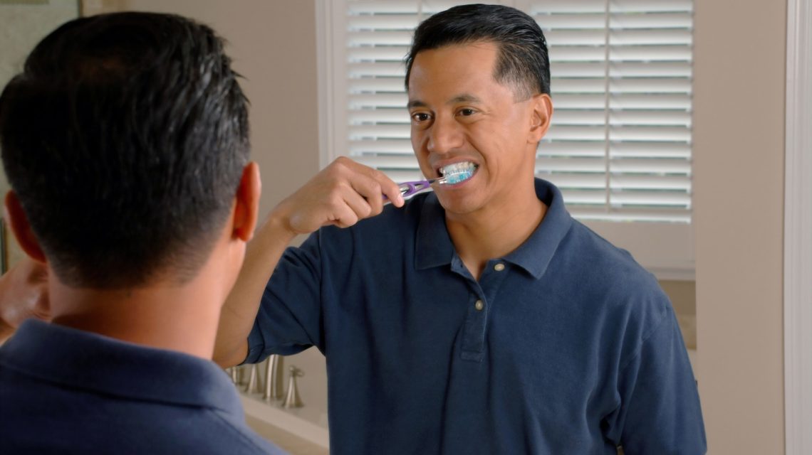 man looking in mirror while brushing teeth